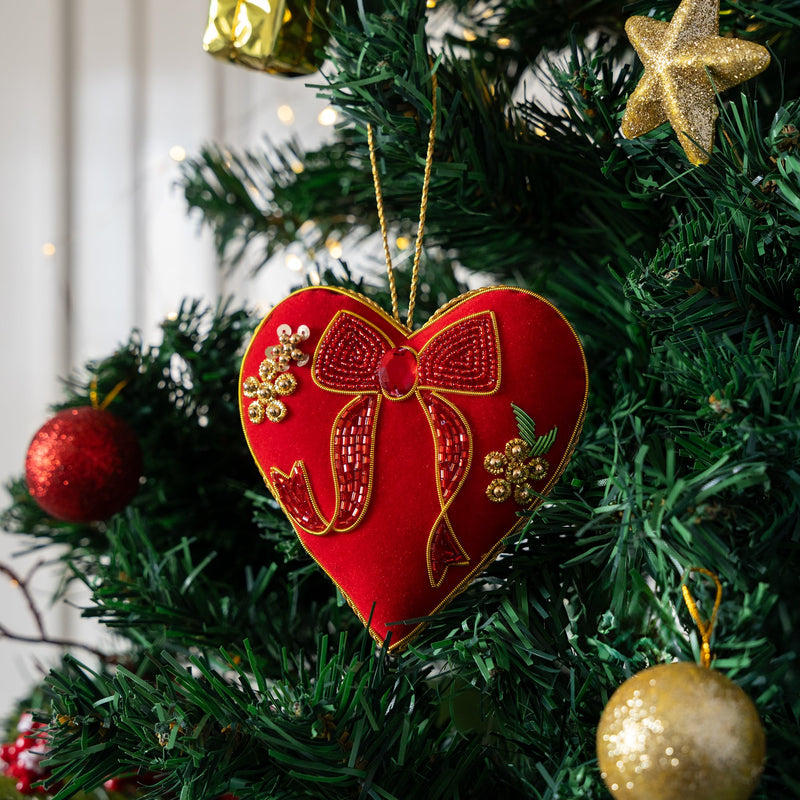 Red heart-shaped ornament with a gold bow on a Christmas tree.