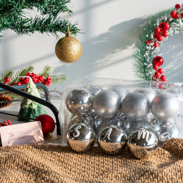 Personalized Christmas baubles set. Assorted shiny metallic ornaments featuring custom initials, stars, and bells in gift packaging